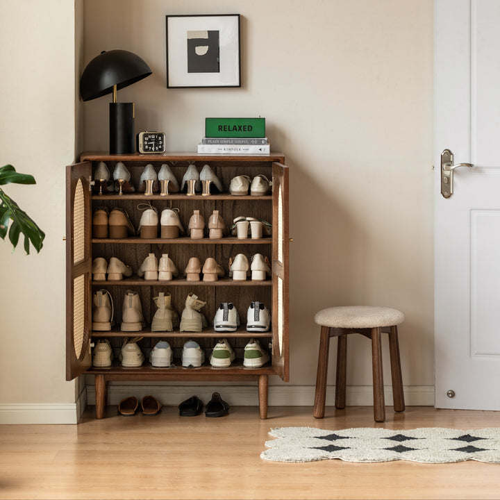 Wooden shoe cabinet with various shoes, a lamp, and books in a room with a door and plant.